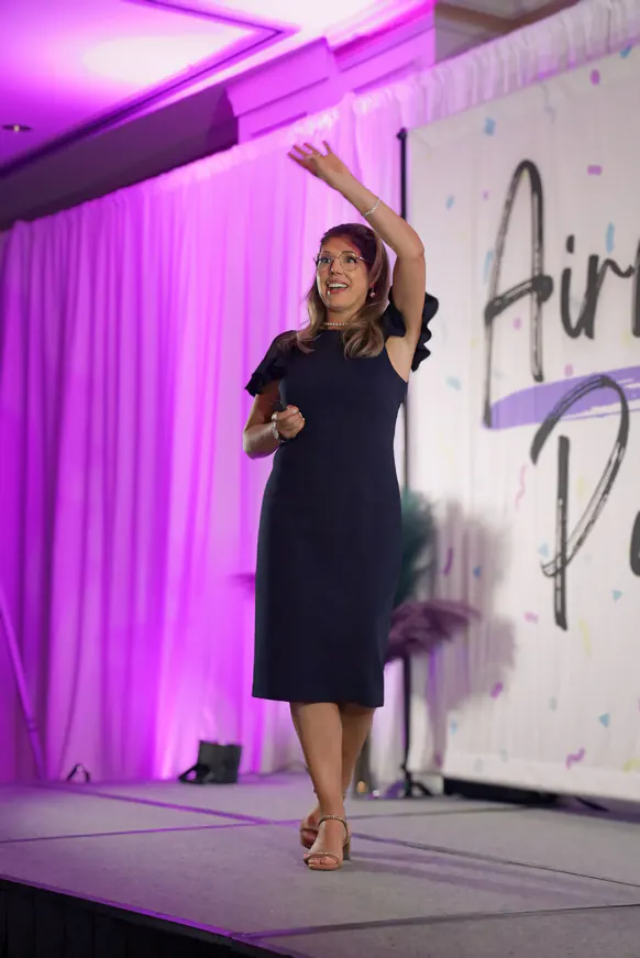 On stage in a blue dress with one hand raised overhead at Airway Palooza 2024